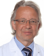 Porträt eines Mannes mit Brille im weißen Kittel und gestreifter Krawatte vor hellem Hintergrund.