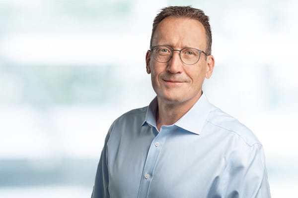 Porträt eines Mannes mit Brille im hellblauen Hemd vor unscharfem Hintergrund.