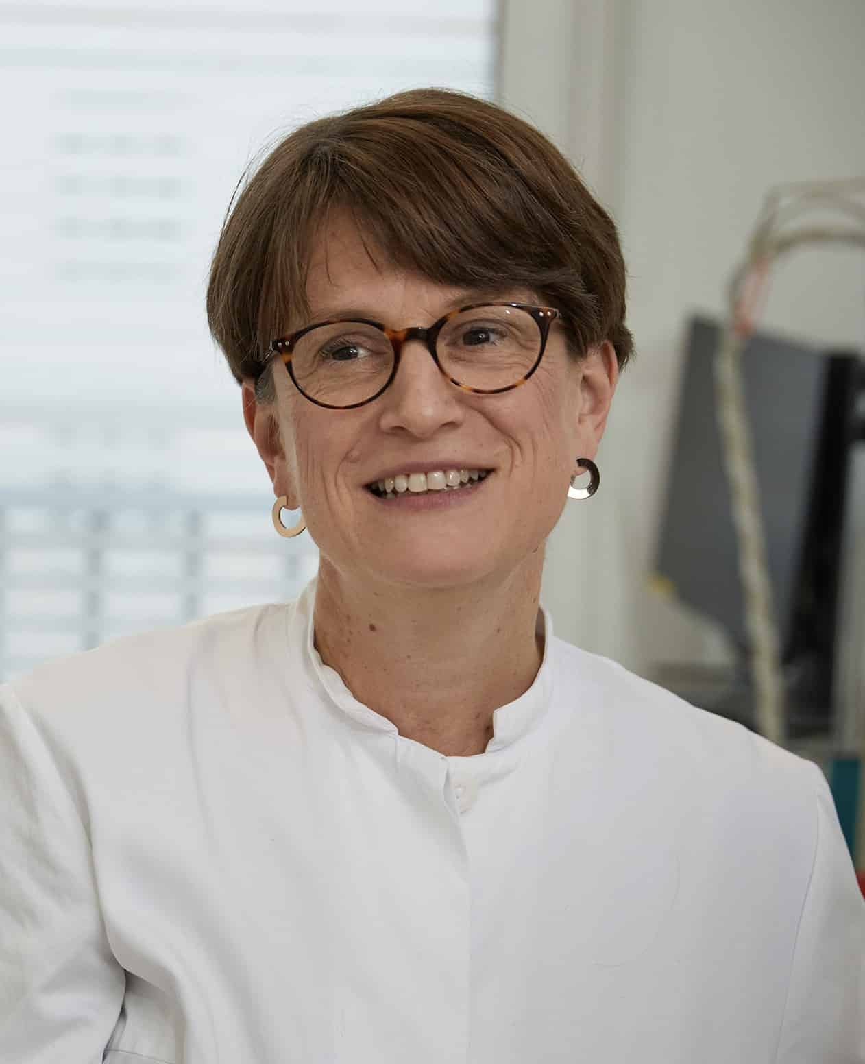 Porträt einer lächelnden Frau mit Brille im weißen Kittel.